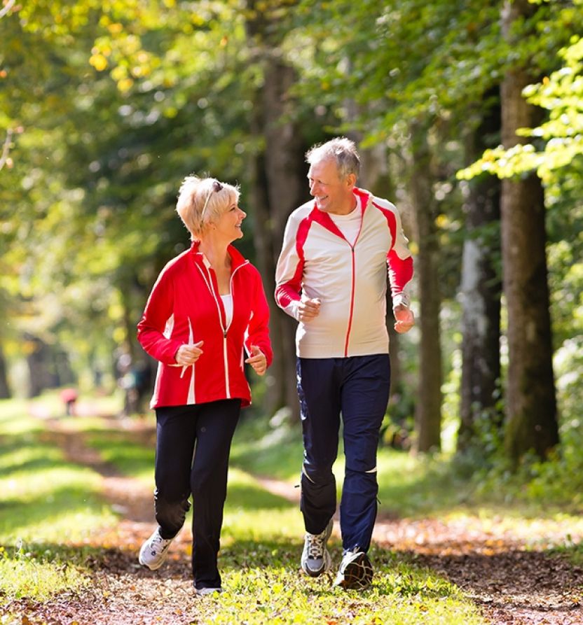 Ein älteres Paar joggt fröhlich durch den Wald und genießt die frische Luft und die Natur um sich herum